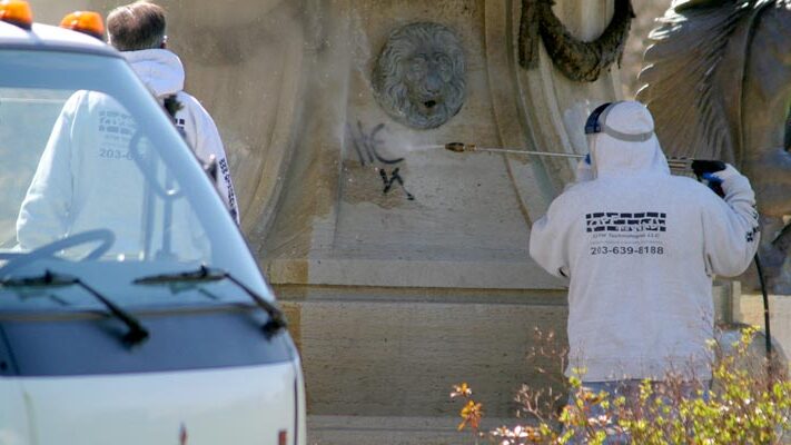 image of a team of graffiti removal specialists using a pressure washer to remove graffiti from the base of a statue
