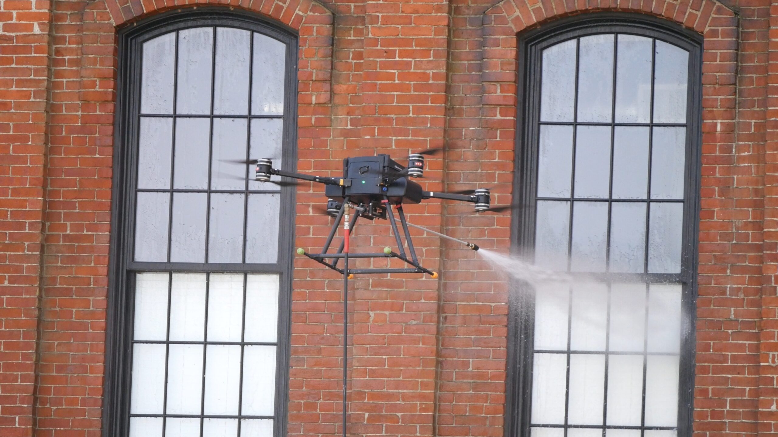 photograph of the OFF THE WALL power washing drone cleaning the windows of an apartment building