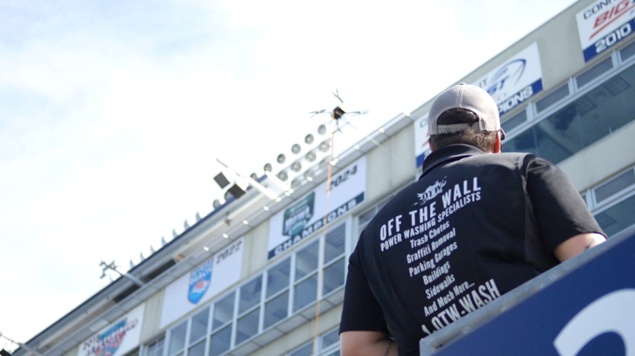 an over-the-shoulder photograph of a trained drone pilot from the OFF THE WALL power washing team guiding the drone carefully across a series of large glass windows