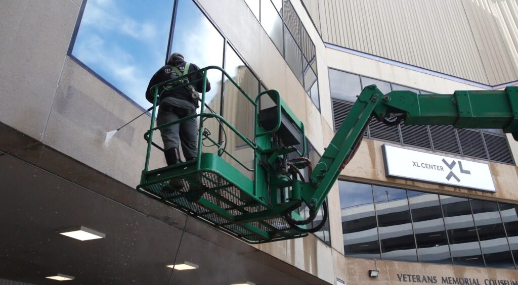 photo of an OFF THE WALL team member on a lift pressure washing the exterior of PeoplesBank Arena in Hartford, CT